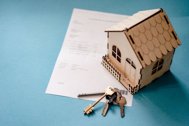 a house figurine next to a contract and keys