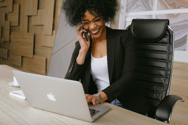 a person smiling while talking on the phone at their desk