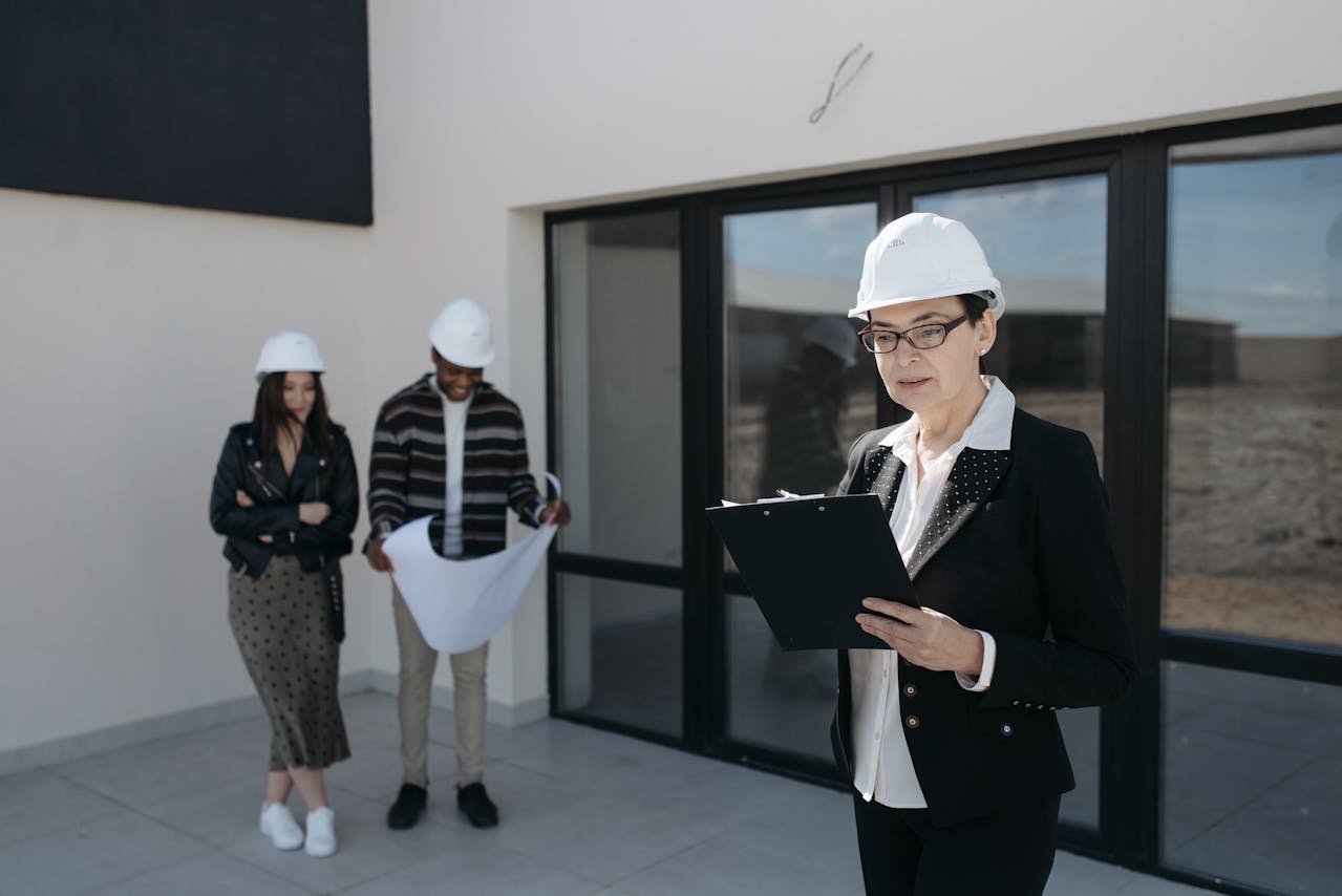 people standing outside of home, with helmets on, one with clipboard